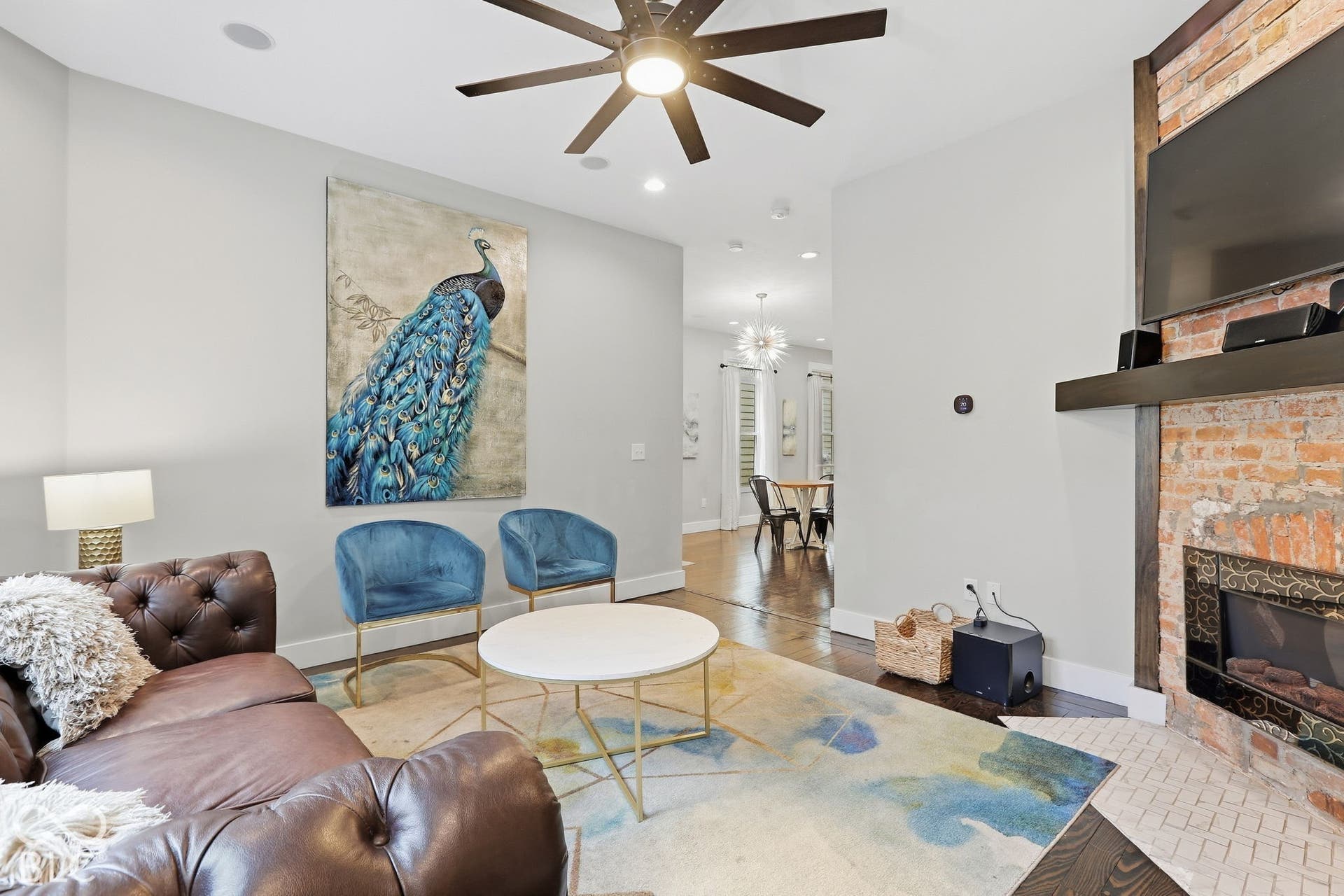 Exposed brick fireplace with a wood mantle, ceiling fan with integrated lighting, recessed lighting, and wood-finish flooring