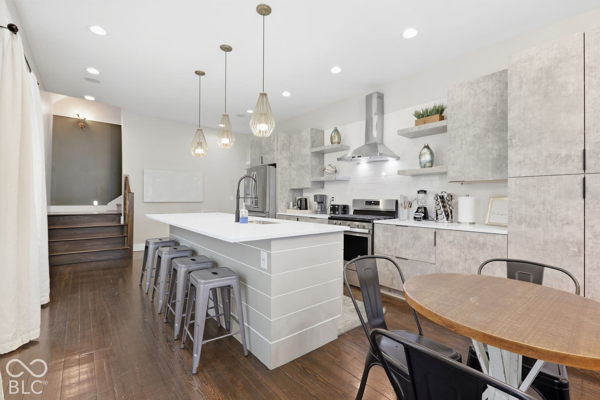 Modern kitchen featuring dark wood-finish flooring, an island with countertop seating, stainless steel appliances, a white tile backsplash, and textured gray cabinetry