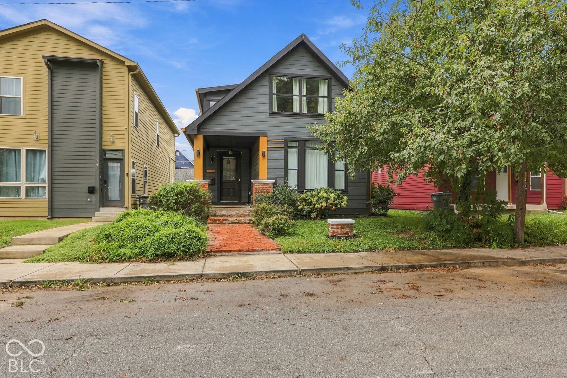 Gray siding exterior with black trim windows, a prominent gable roof, and a red brick path leading to the entrance