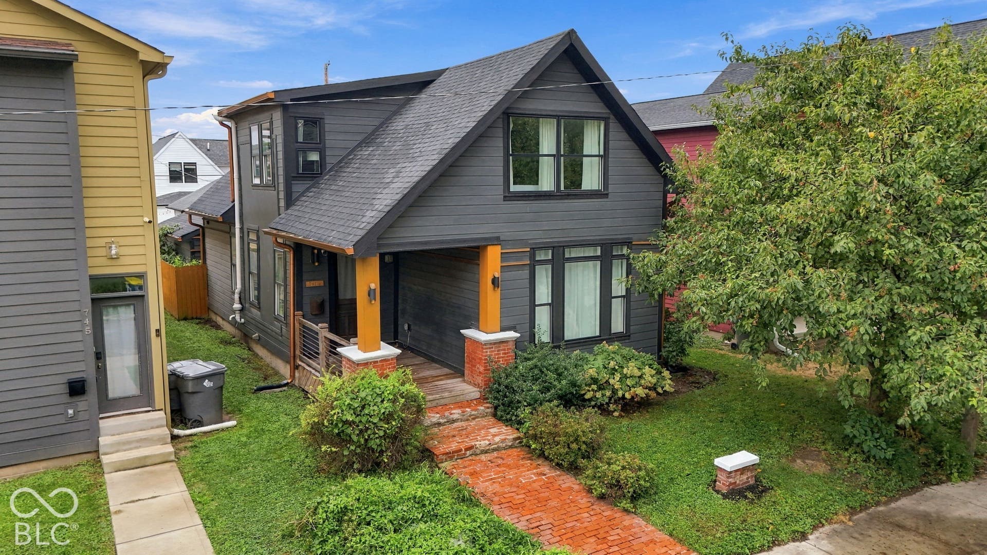 Modern-style exterior with dark siding, prominent gabled roofline, and front porch featuring wood columns and brick bases