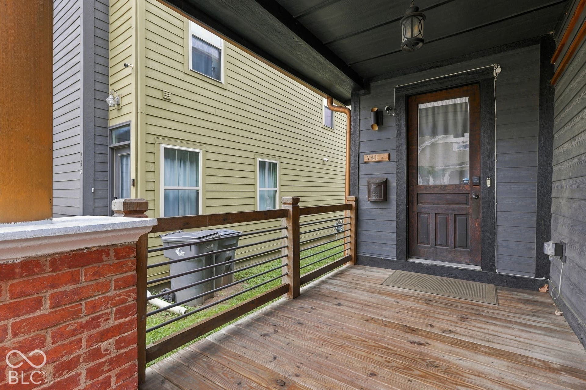 Covered front porch with wood flooring, red brick detailing, wood and metal railings, and a solid wood entry door