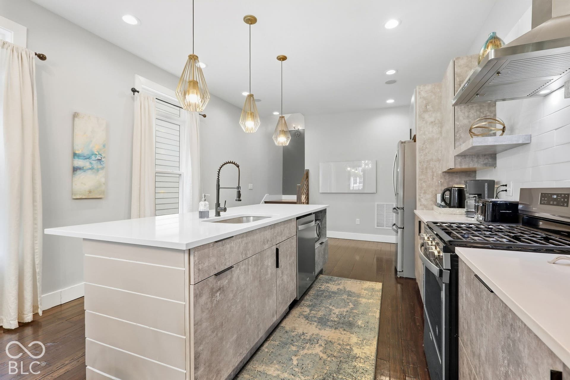 Central island with integrated sink, stainless steel appliances, wood-finish flooring, white countertops, and contemporary pendant lighting