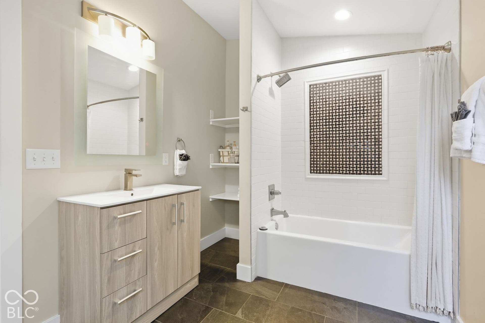Bathroom featuring a light wood-finish vanity with an integrated sink, gold-tone faucet, and a large mirror with overhead lighting