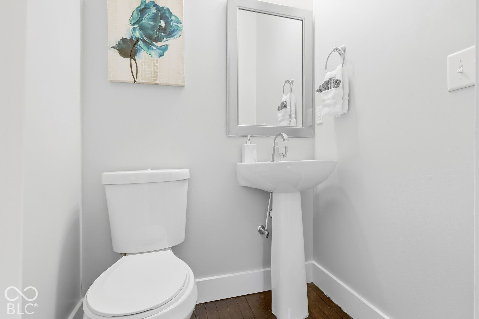 Pedestal sink with chrome-finish faucet, framed mirror, and wood-finish flooring