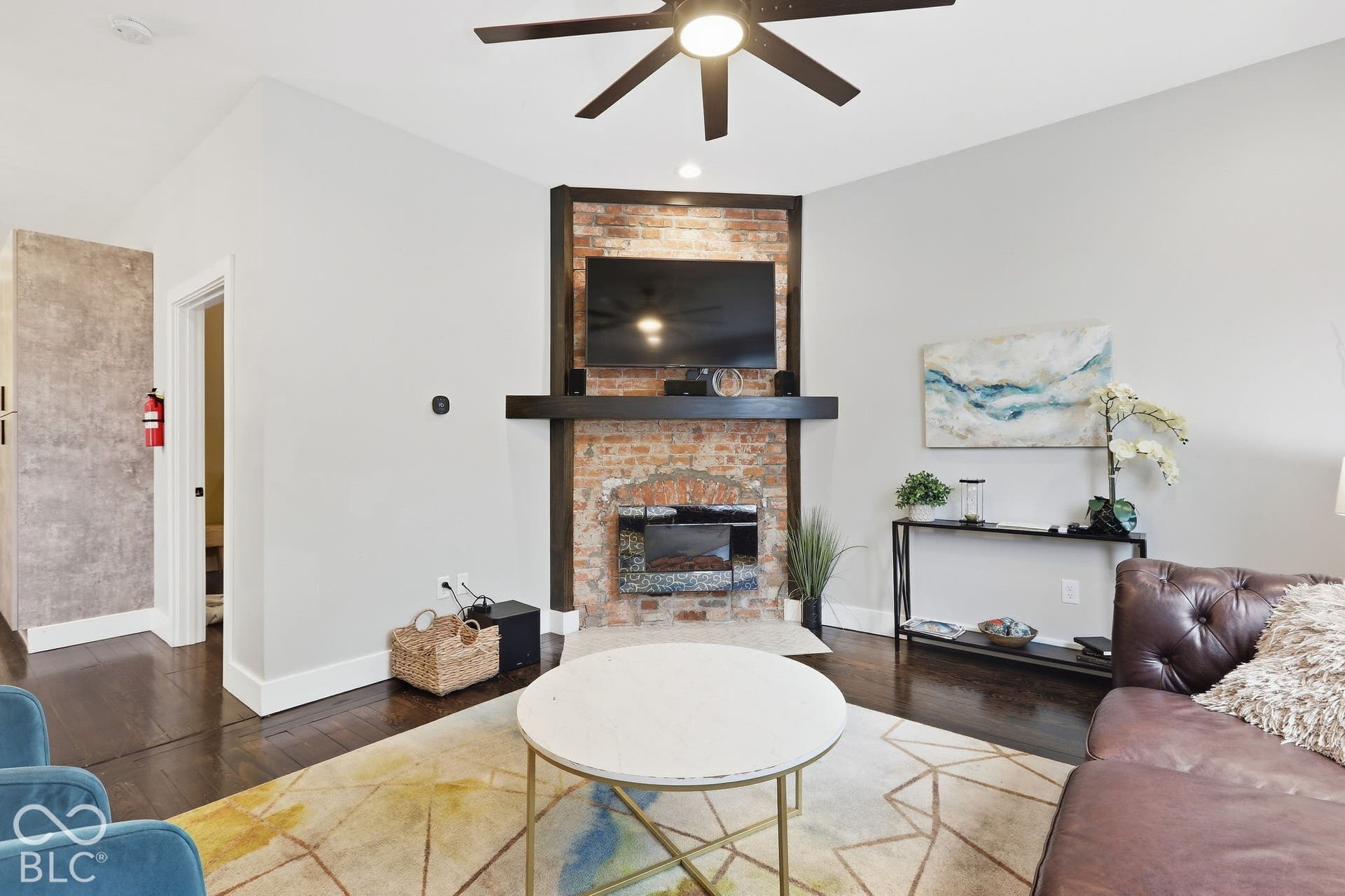 Exposed brick fireplace with a wood mantel, dark wood-finish flooring, and a ceiling fan
