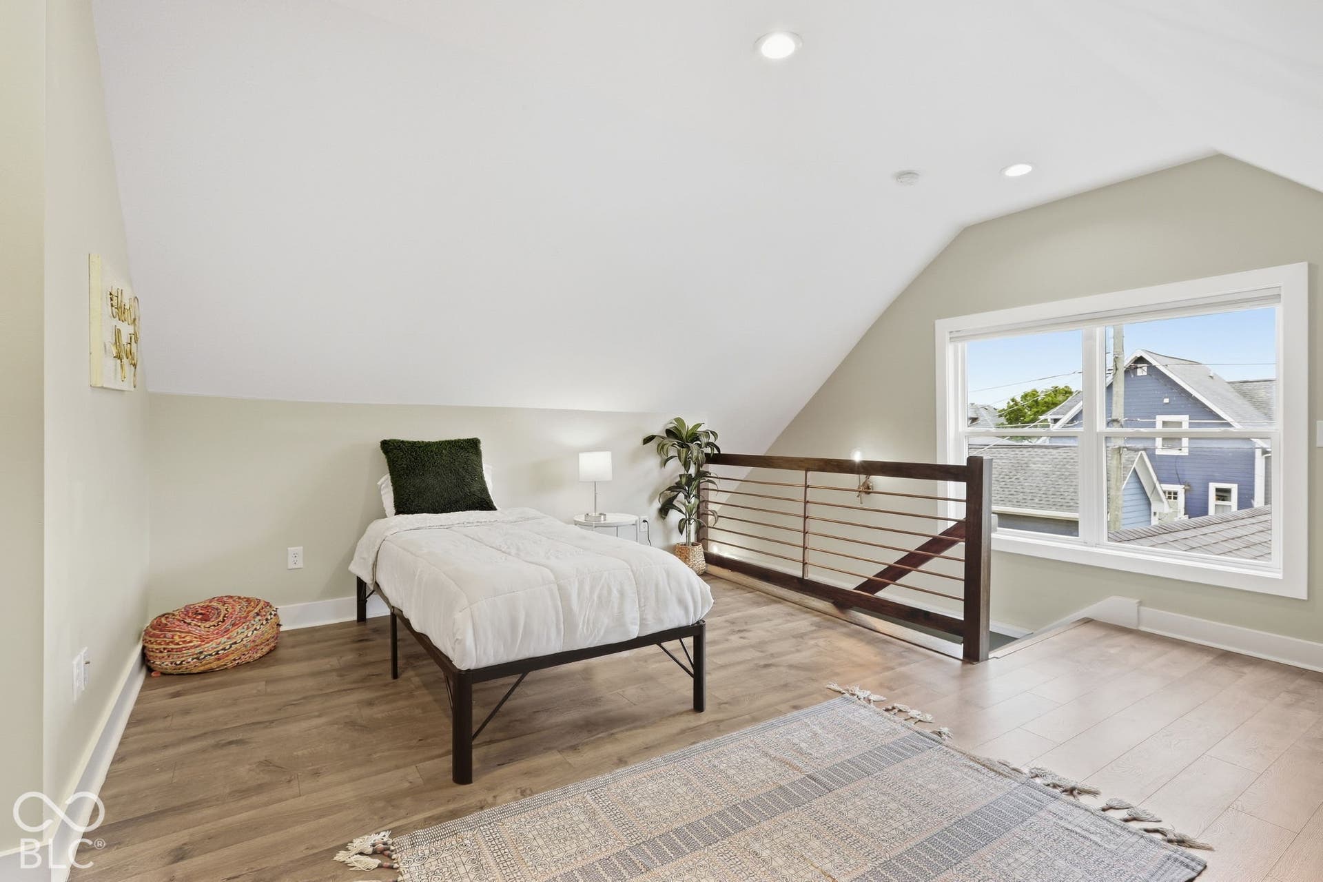 Angled ceiling loft space featuring wood-finish flooring, recessed lighting, and a modern horizontal slat railing