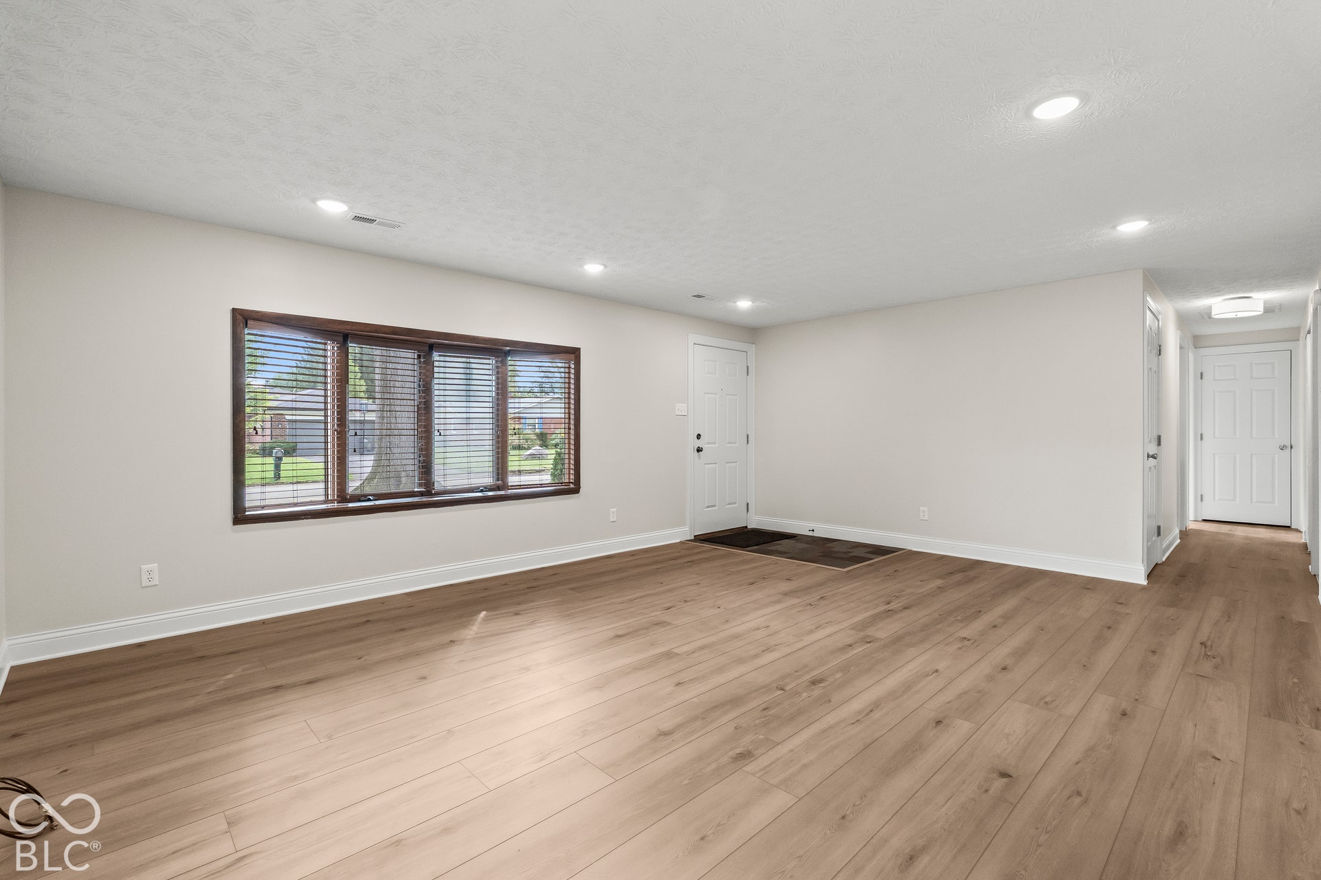 Spacious room featuring wood-finish flooring, recessed lighting, a front entry door with a multi-pane window, and a large bay window with dark trim