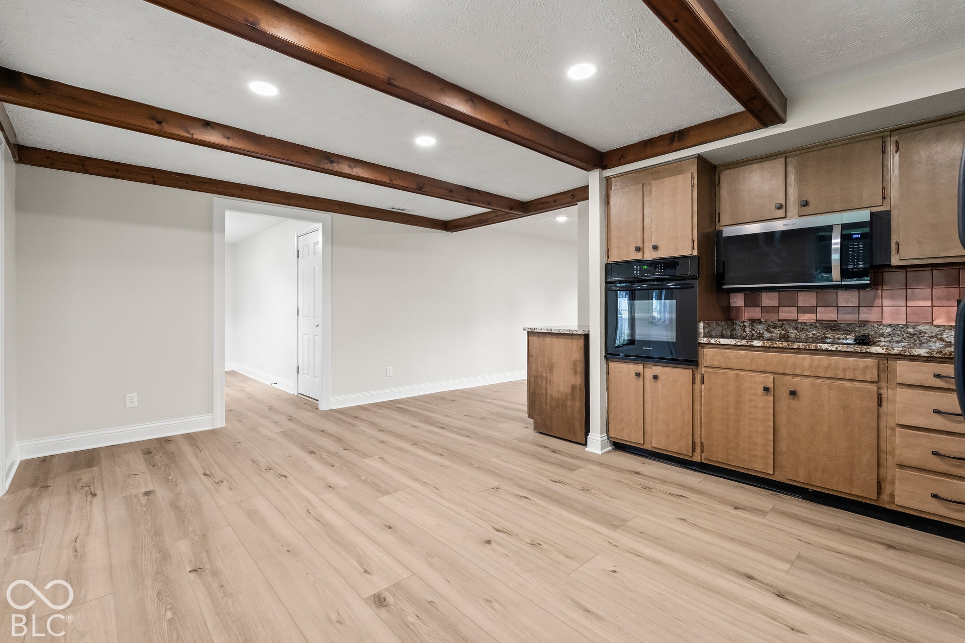 Wood-finish flooring throughout, exposed ceiling beams, recessed lighting, built-in wall oven, and stainless steel microwave