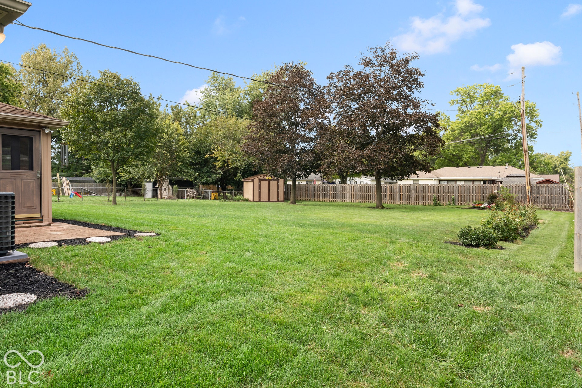 Expansive grassy yard with mature trees, a privacy fence, and a patio area
