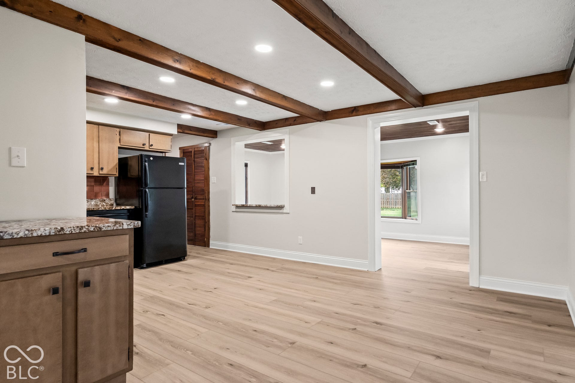 Wood-finish flooring throughout, exposed ceiling beams, recessed lighting, shaker-style cabinetry, and a kitchen pass-through