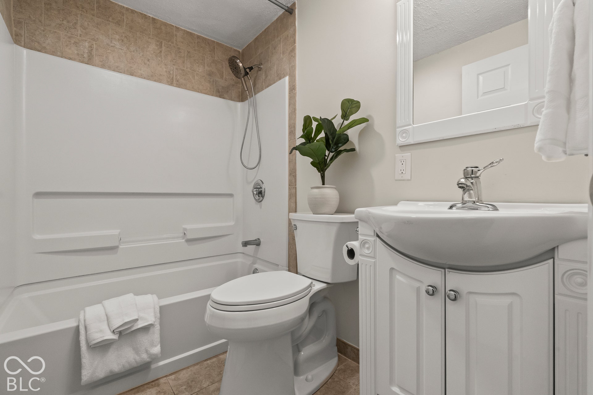 White bathtub with an integrated shower, chrome fixtures, and a tiled shower surround