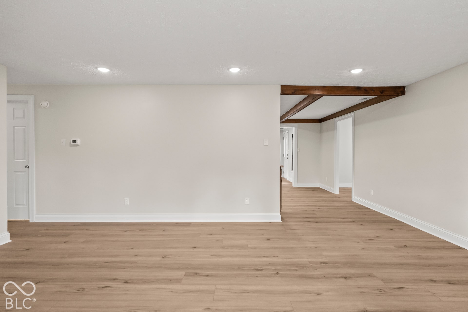 Wood-finish flooring throughout, recessed lighting, white baseboards, and exposed wood beams