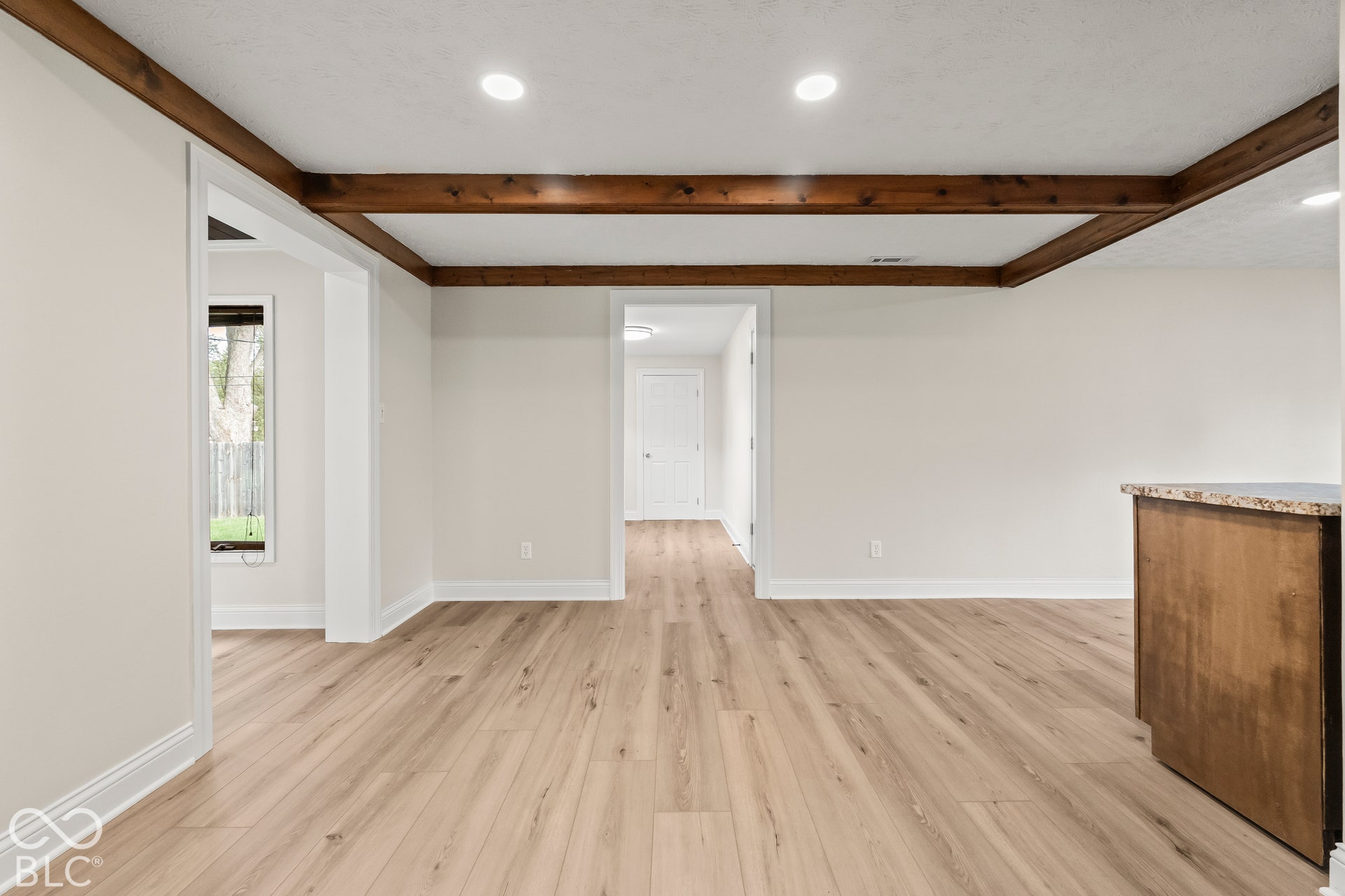 Wood-finish flooring with recessed lighting and exposed wood ceiling beams