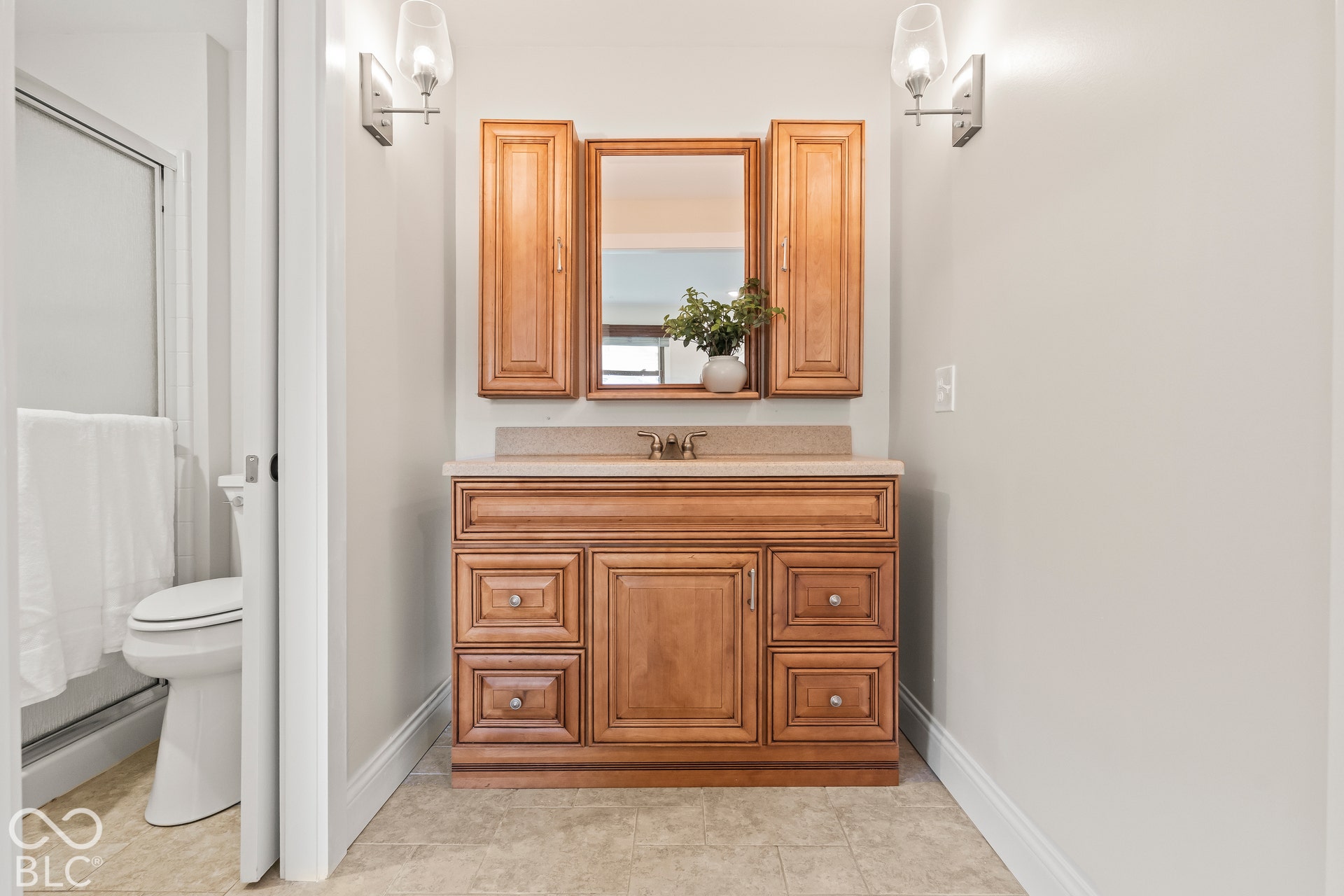 Wood-finish vanity with a stone-finish countertop, undermount sink, and wall-mounted sconce lighting