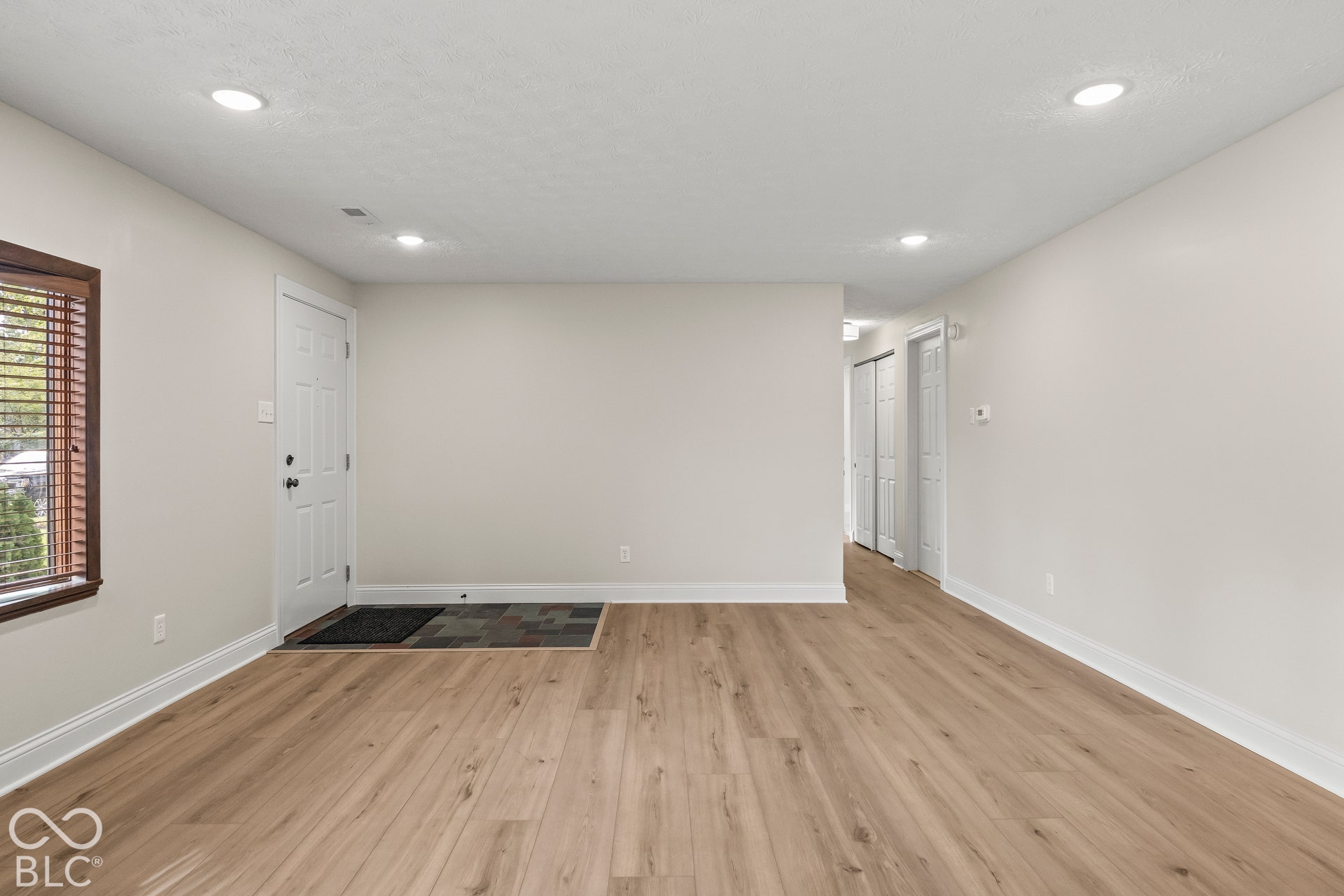 Wood-finish flooring throughout, recessed ceiling lighting, window with wood-finish blinds, white interior doors, and white baseboards