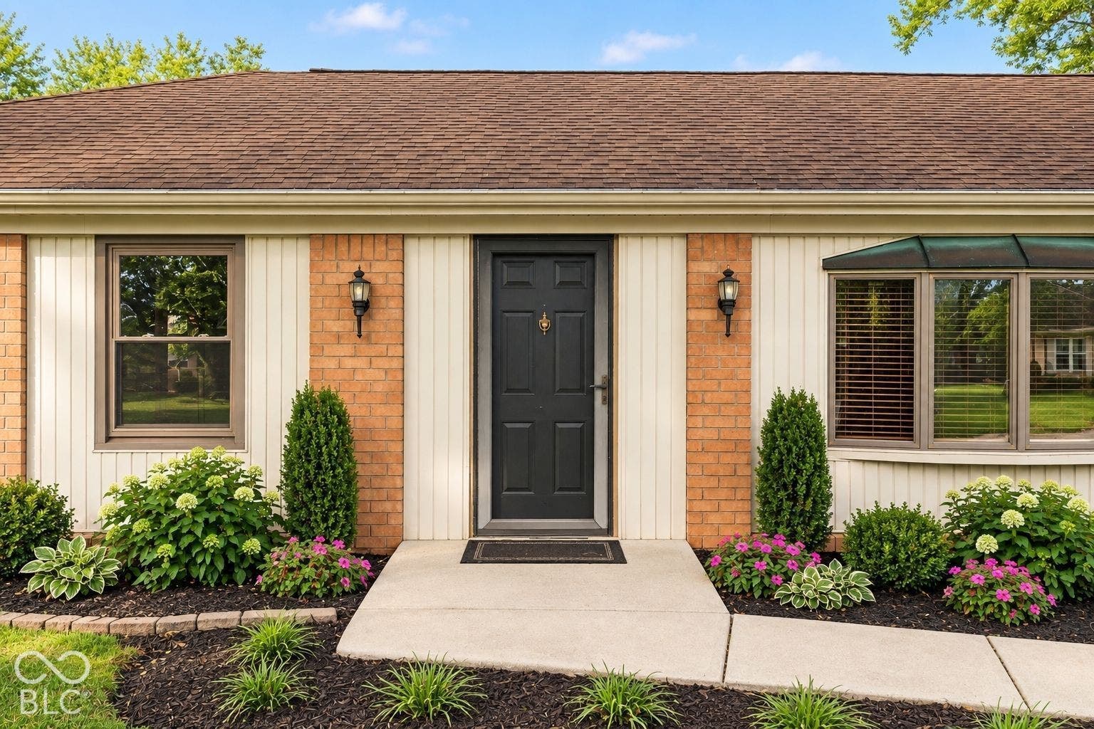 Brick and vertical siding exterior with a dark entry door, symmetrical wall sconces, and a bay window featuring a copper-toned awning