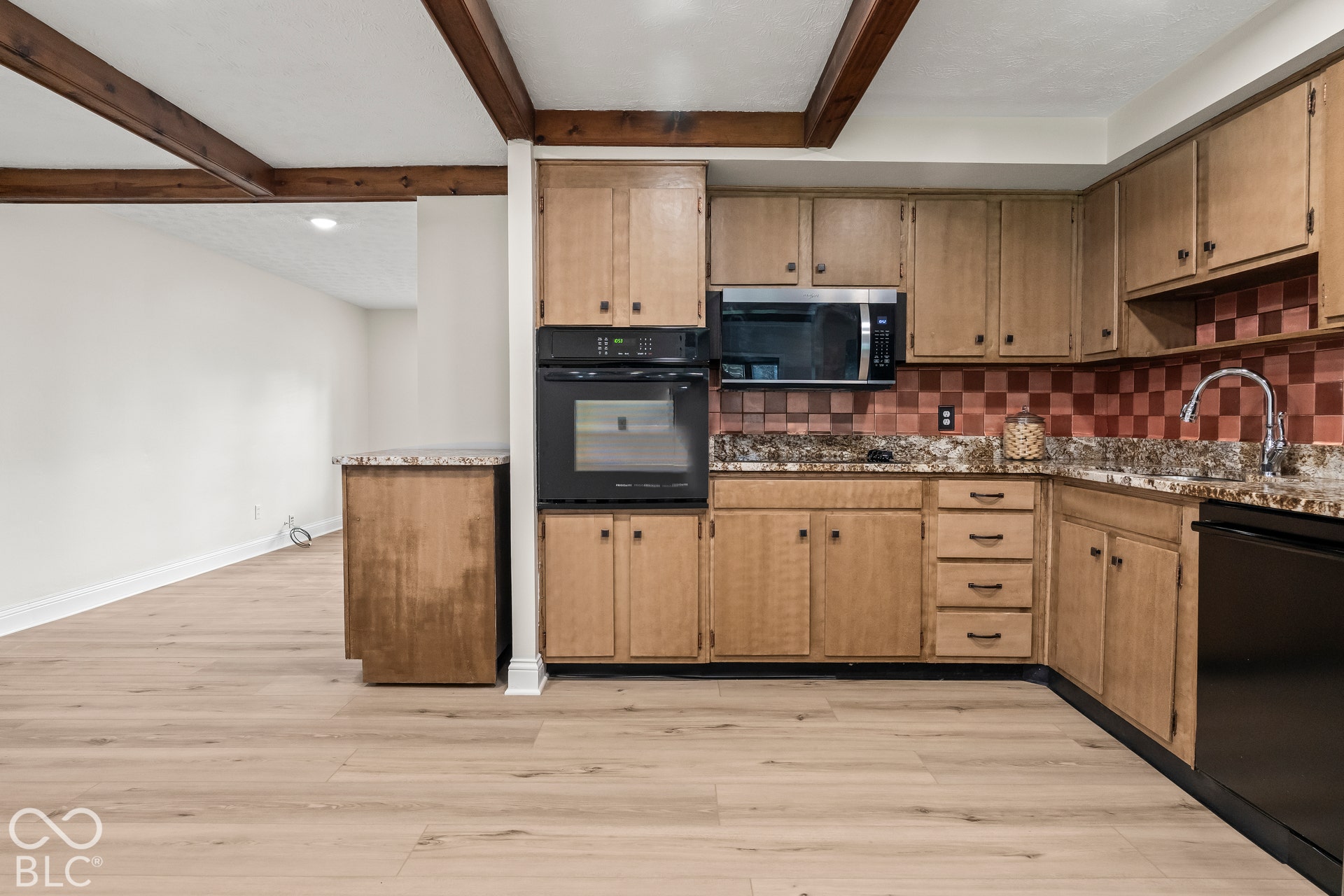 Kitchen featuring wood-finish cabinetry, built-in microwave, integrated oven, granite-style countertops, and a checkered tile backsplash