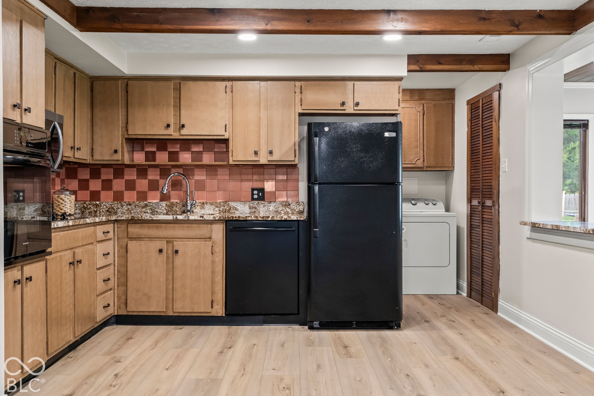 Kitchen with wood-finish flooring, exposed ceiling beams, wood cabinetry, and a checkerboard pattern backsplash
