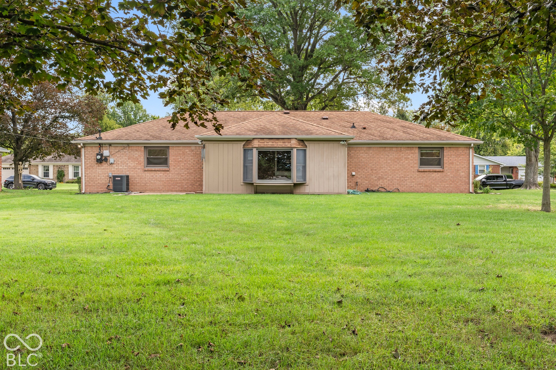 Expansive lawn with mature trees, brick exterior, bay window with shutters, and a shingle roof