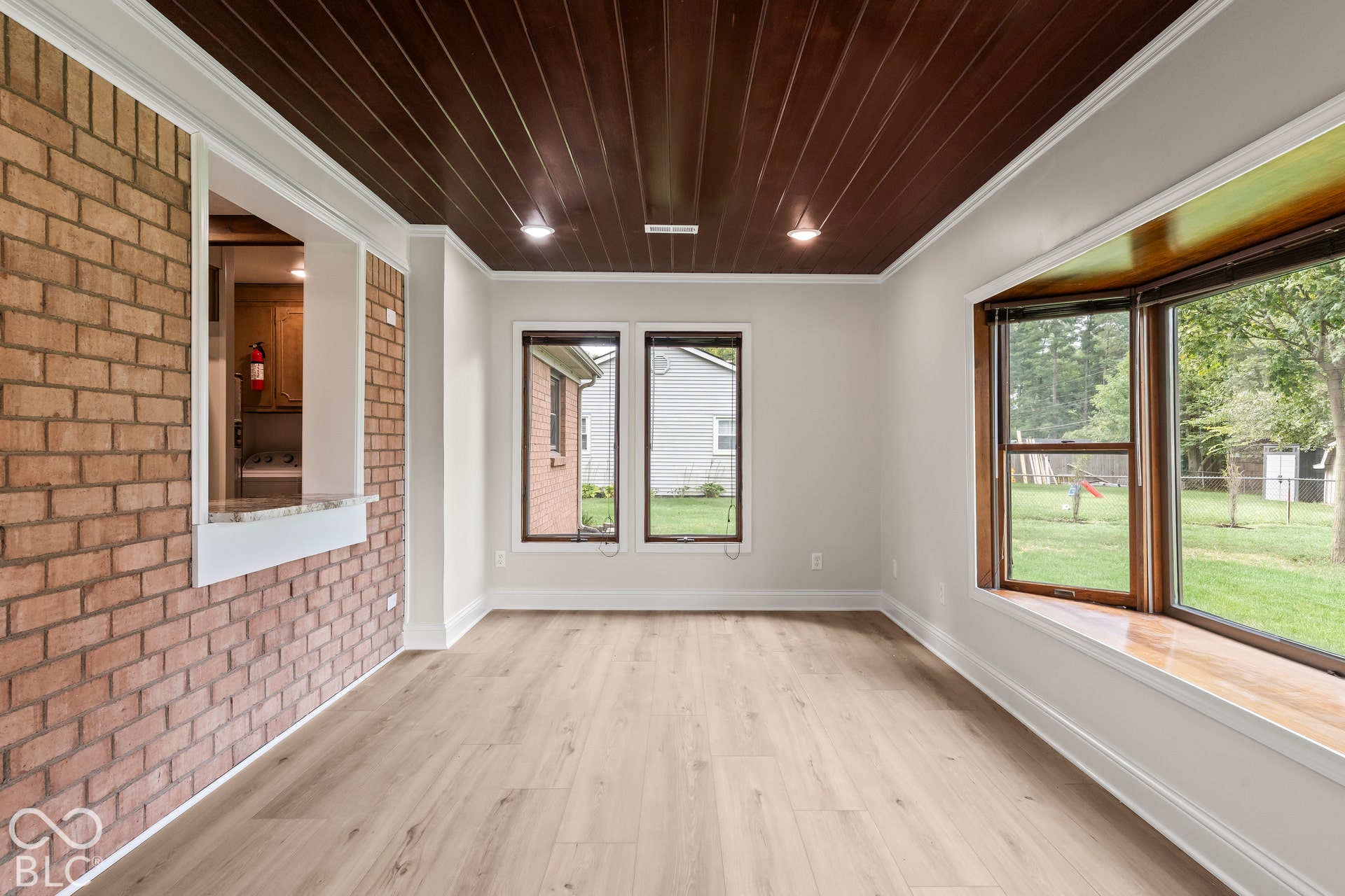 Wood-finish flooring, brick-accented wall, wood-paneled ceiling with recessed lighting, and a bay window