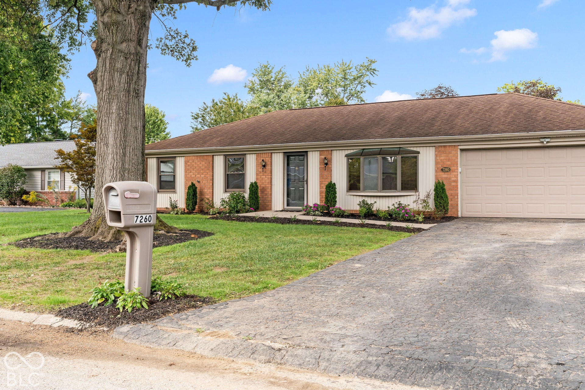 Brick and siding exterior featuring a two-car garage, mature landscaping, and a bay window