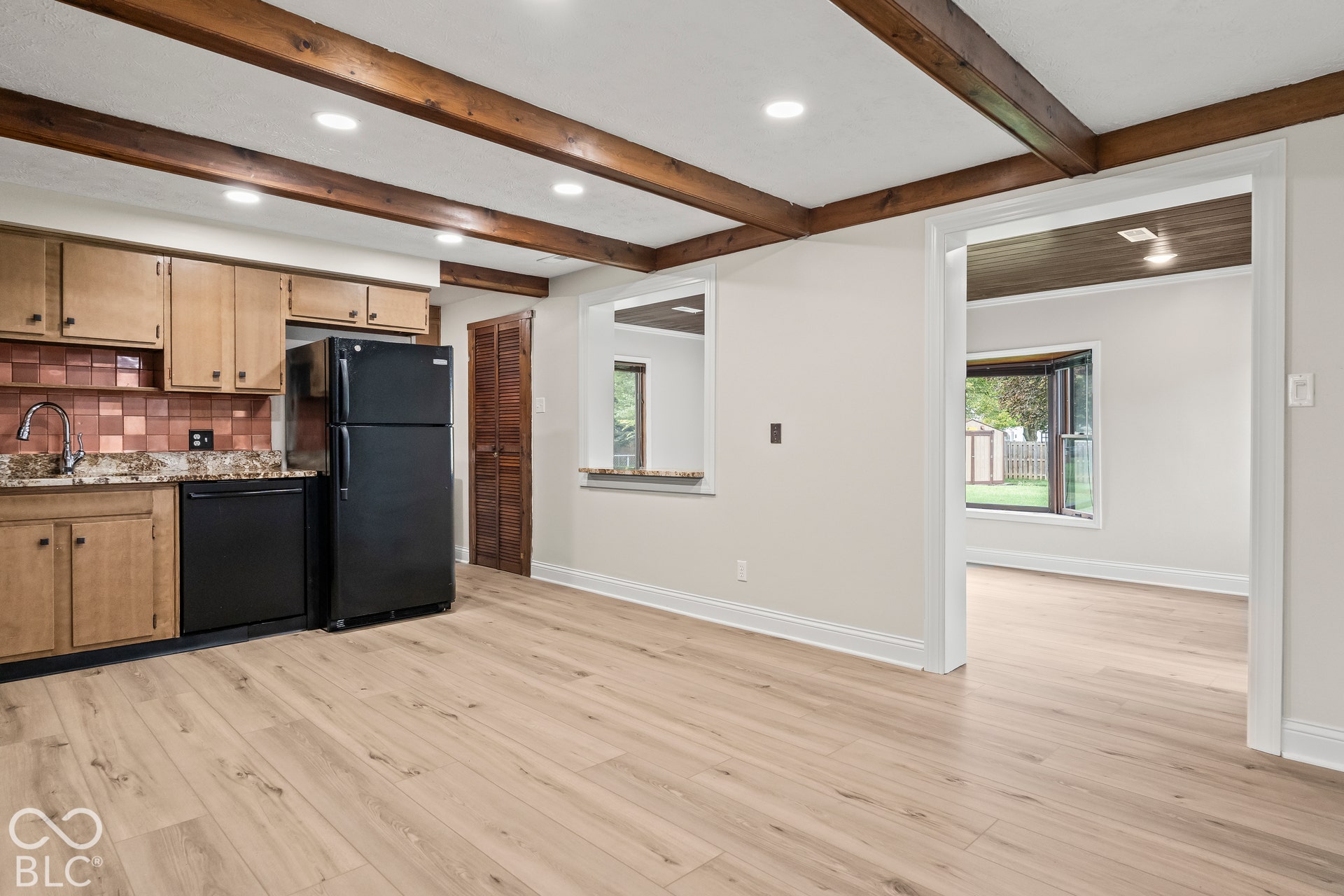 Wood-finish flooring, exposed ceiling beams, recessed lighting, and a kitchen with wood cabinetry and dark countertops