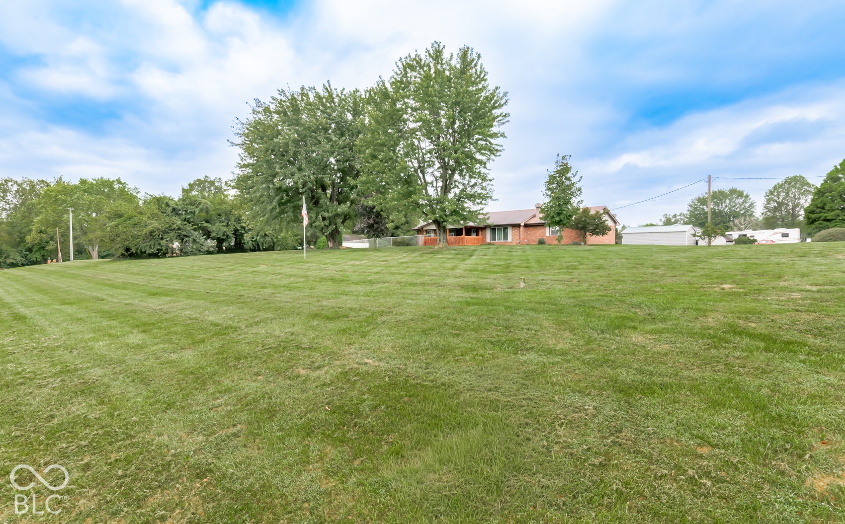 Expansive green lawn, mature trees, brick exterior, covered porch, detached structure