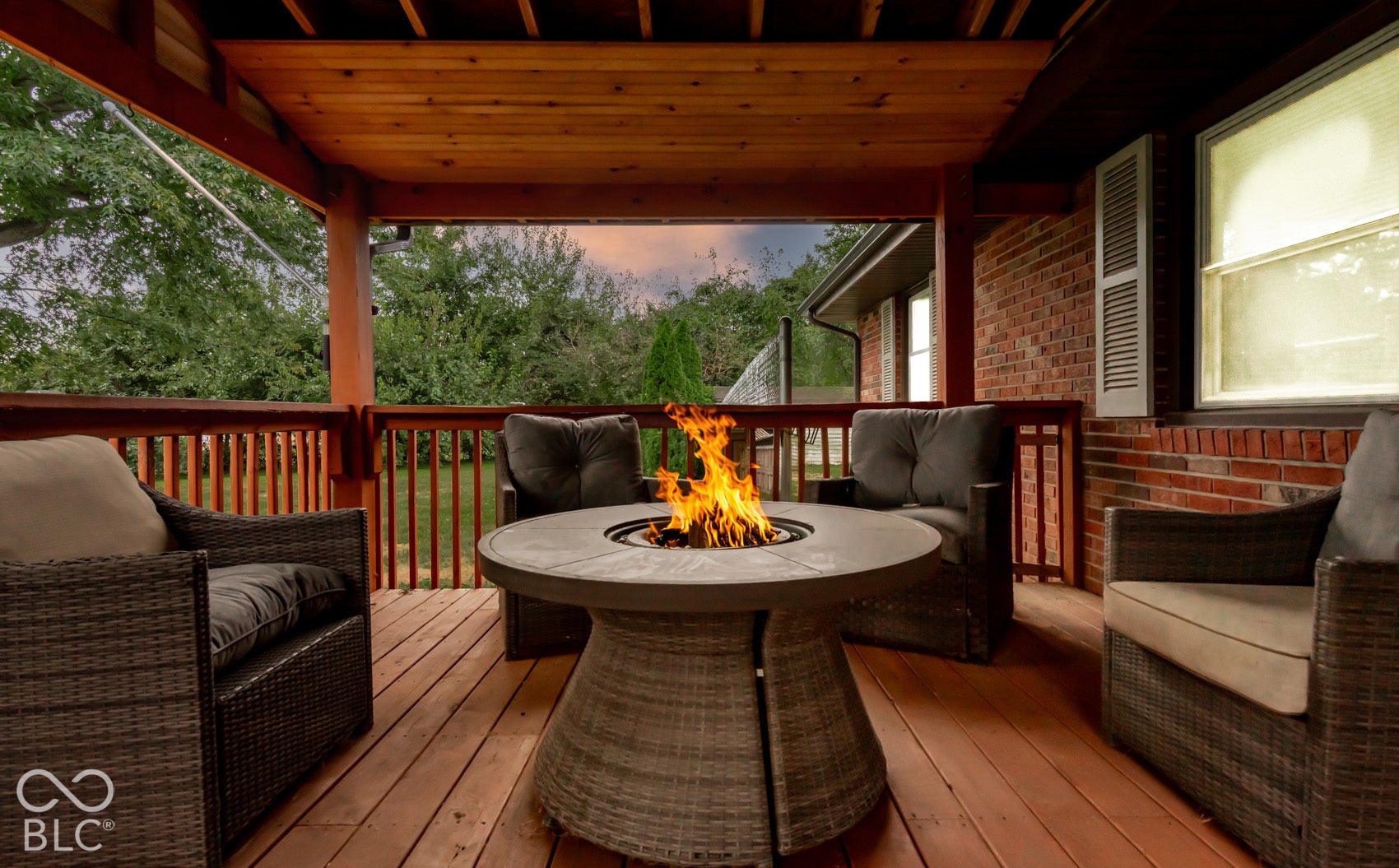Covered wood deck featuring a fire pit, wood railing, and brick exterior