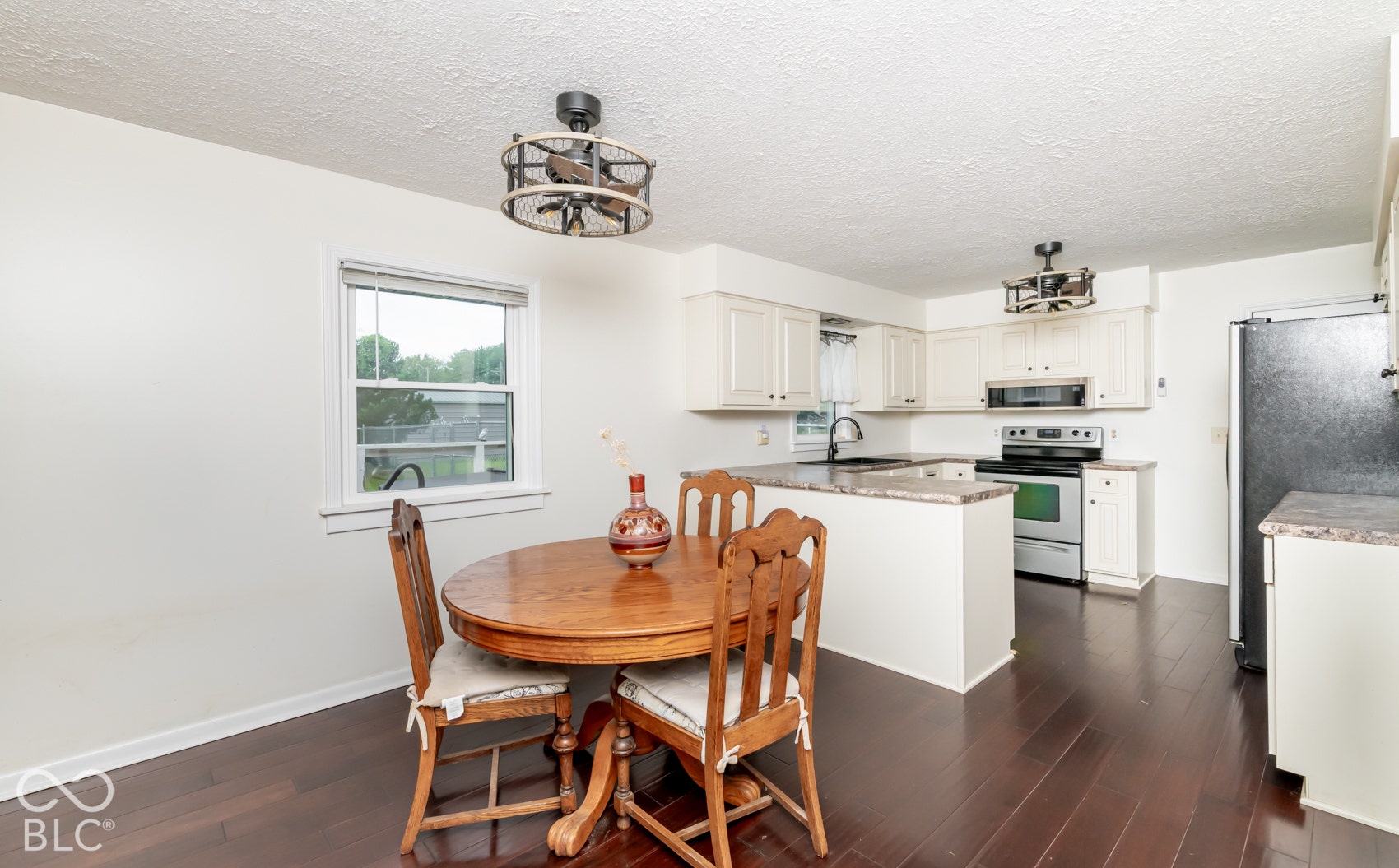 Wood-finish flooring throughout, white cabinetry with dark hardware, stainless steel appliances, and a breakfast bar