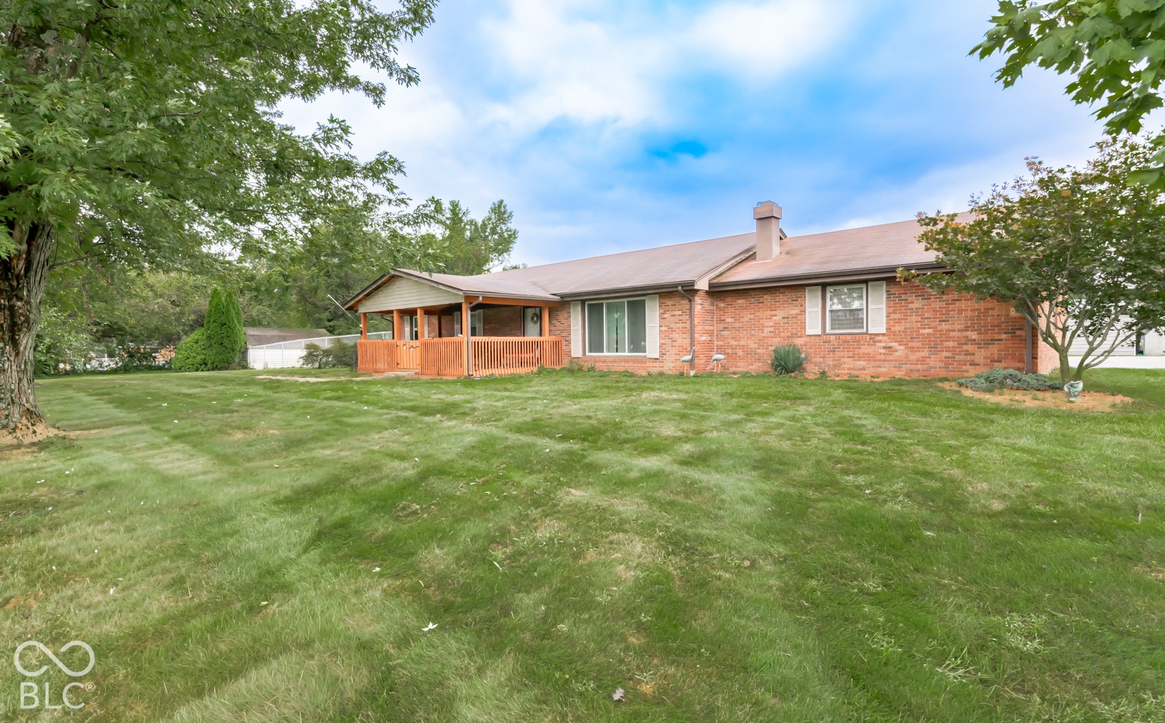 Brick exterior with a covered porch, wood railing, and a large lawn
