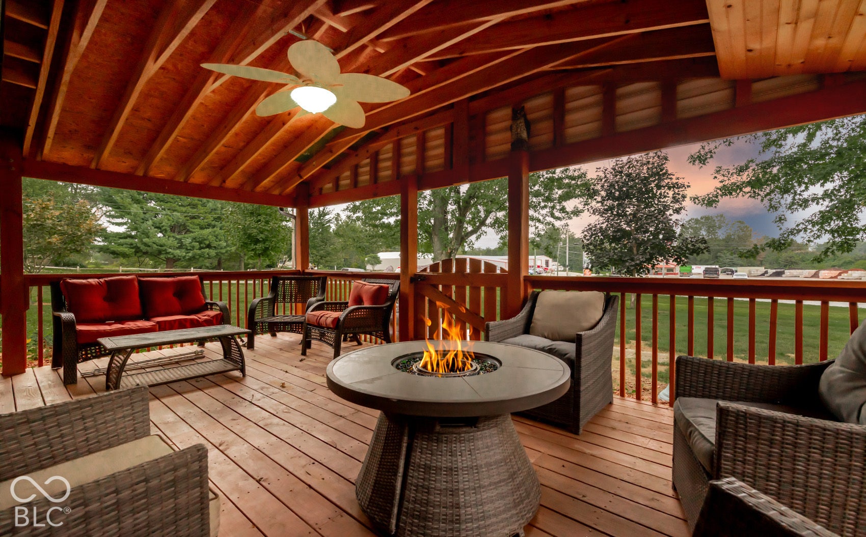 Expansive wooden deck featuring a slatted wood ceiling, built-in ceiling fan, wood-finish flooring, and a stone-finish fire pit