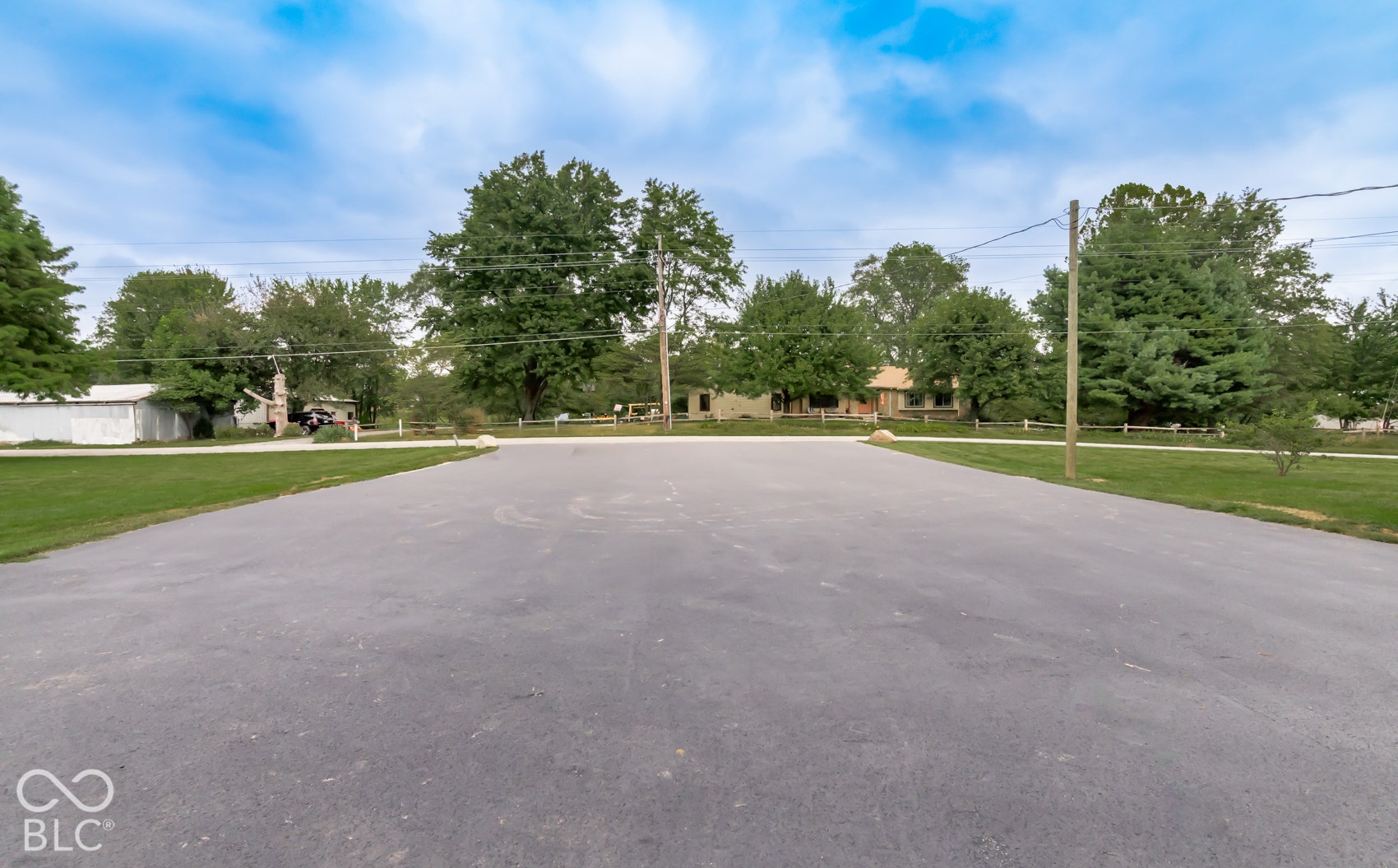 Asphalt driveway with surrounding green lawn and mature trees