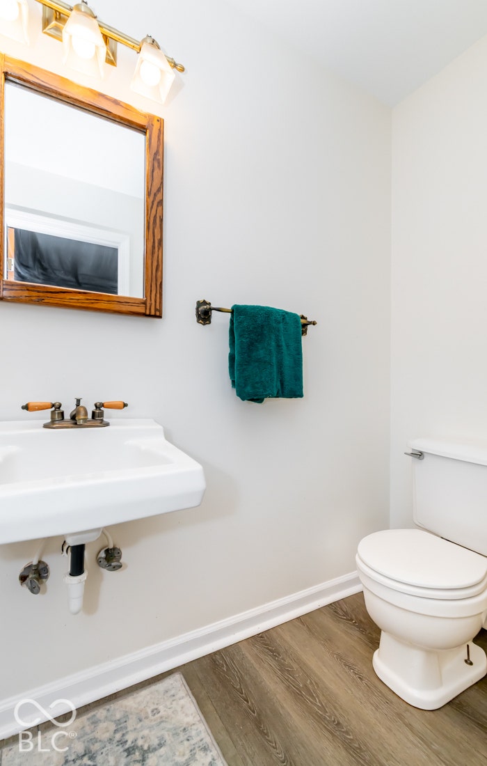 Wall-mounted sink with brass-finish faucet, framed mirror, wall-mounted light fixture, and wood-finish flooring