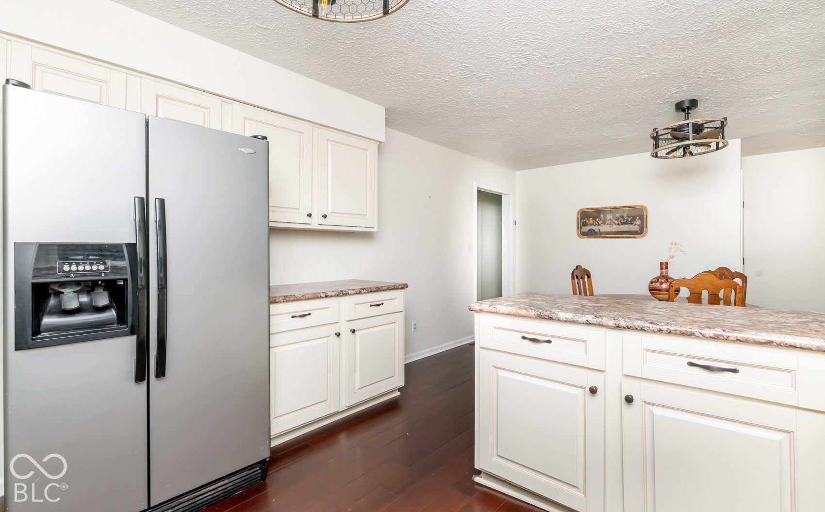 White cabinetry, stainless steel refrigerator, dark wood-finish flooring, and a kitchen island with a stone-finish countertop