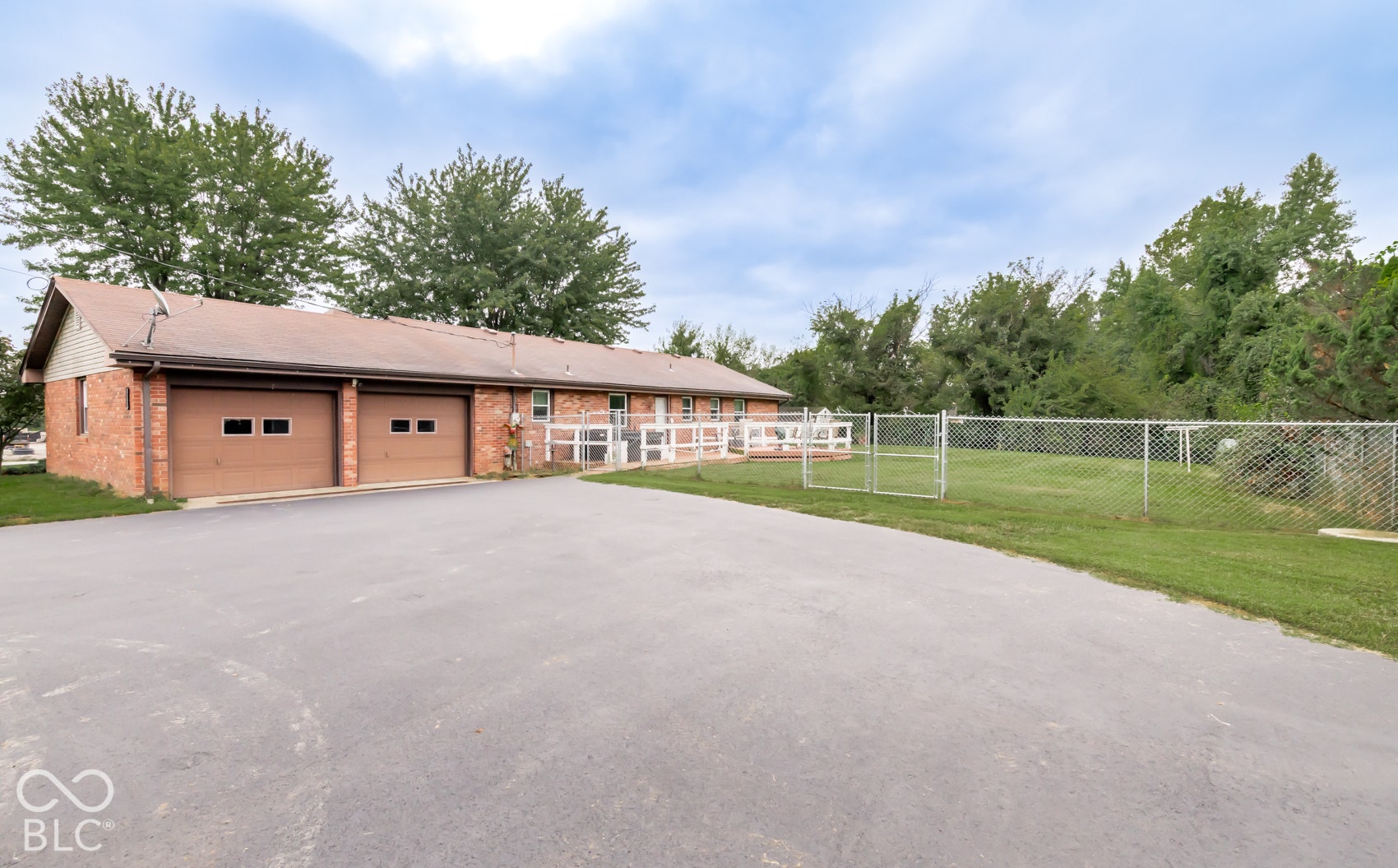 Brick exterior with two attached garages, a paved driveway, and a chain-link fence enclosing a grassy area