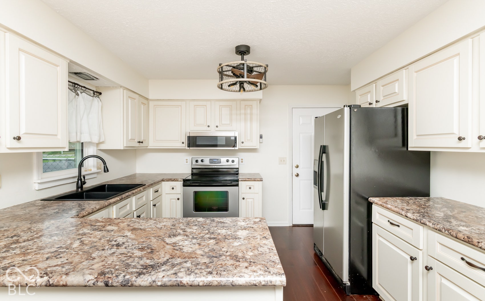 White cabinetry, stainless steel appliances, dark wood-finish flooring, and multi-toned countertops