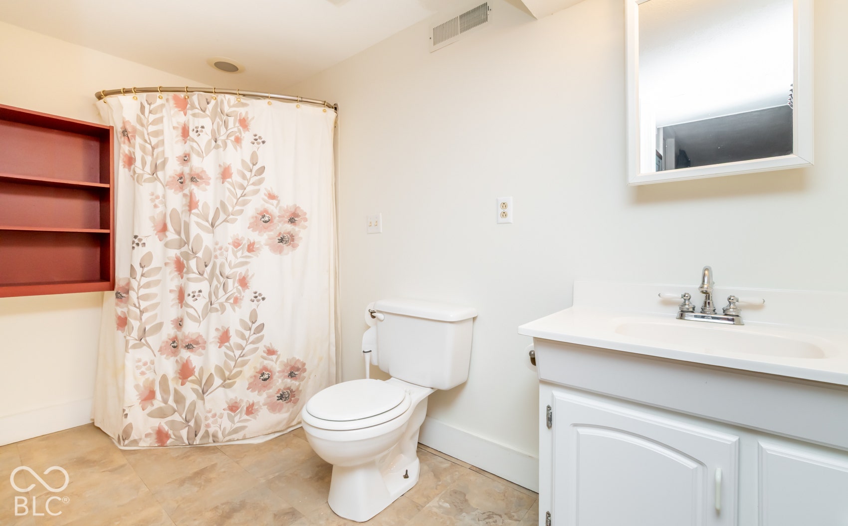 Bathroom featuring a shower with curved rod, built-in wall shelving, vanity with integrated sink, wall-mounted mirror, and tile flooring