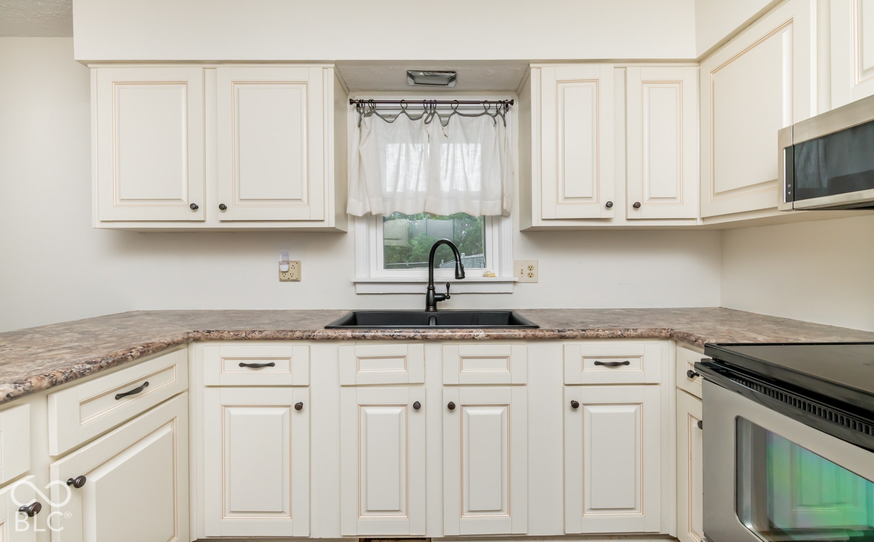 Kitchen featuring cream cabinetry, dark countertops, a black basin sink, a black gooseneck faucet, and a stainless steel microwave