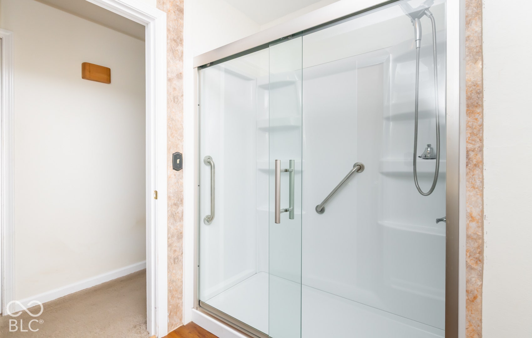 Shower enclosure with clear glass doors, white shower surround, and integrated shelving