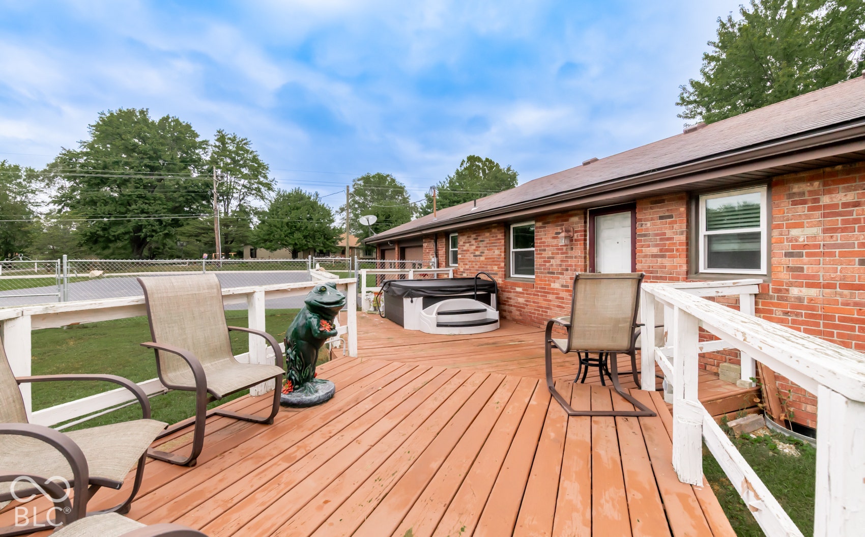 Expansive wood-finish deck with white railings, featuring an integrated hot tub and red brick exterior