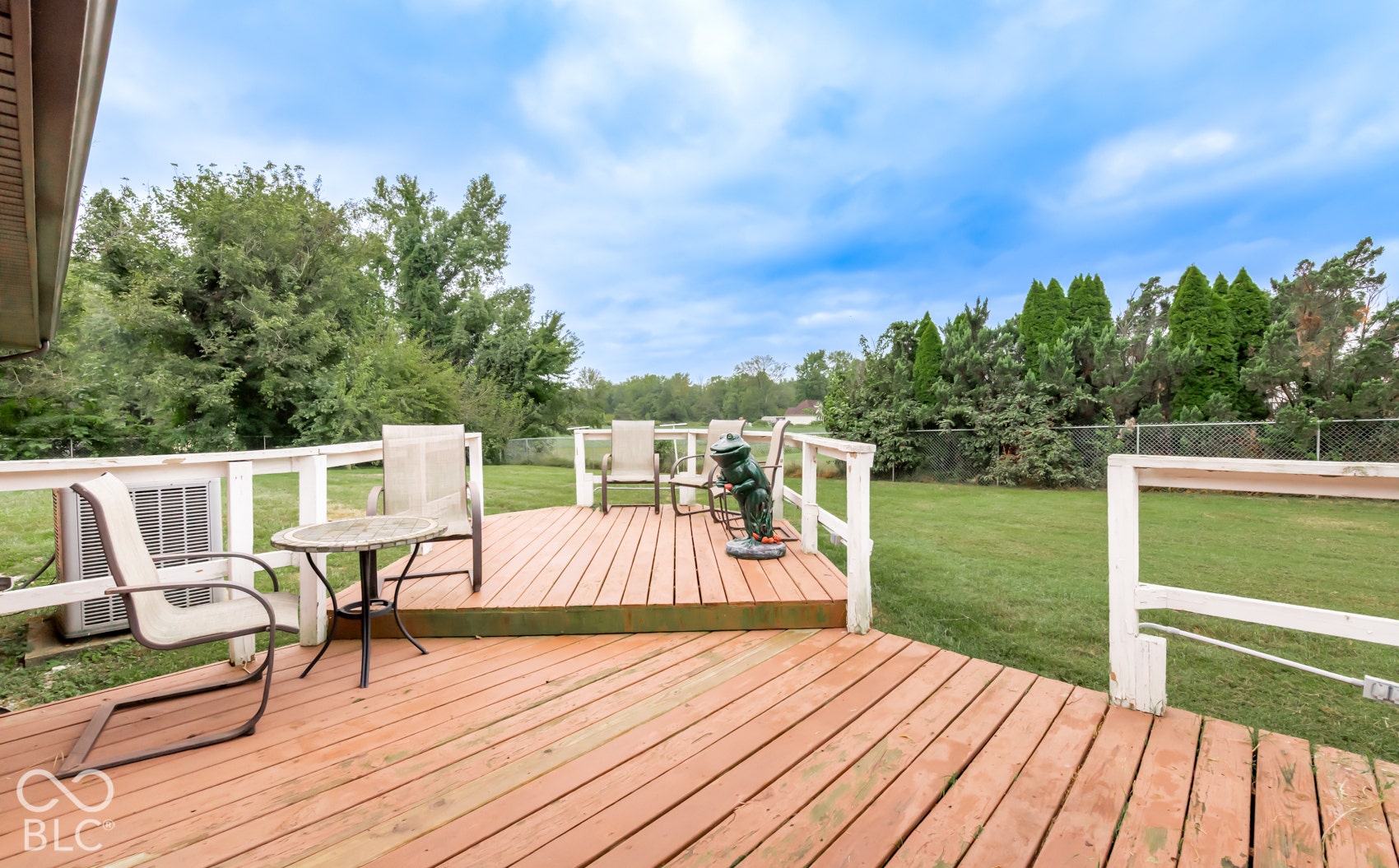 Wood deck with white railing, featuring a spacious lawn and mature trees