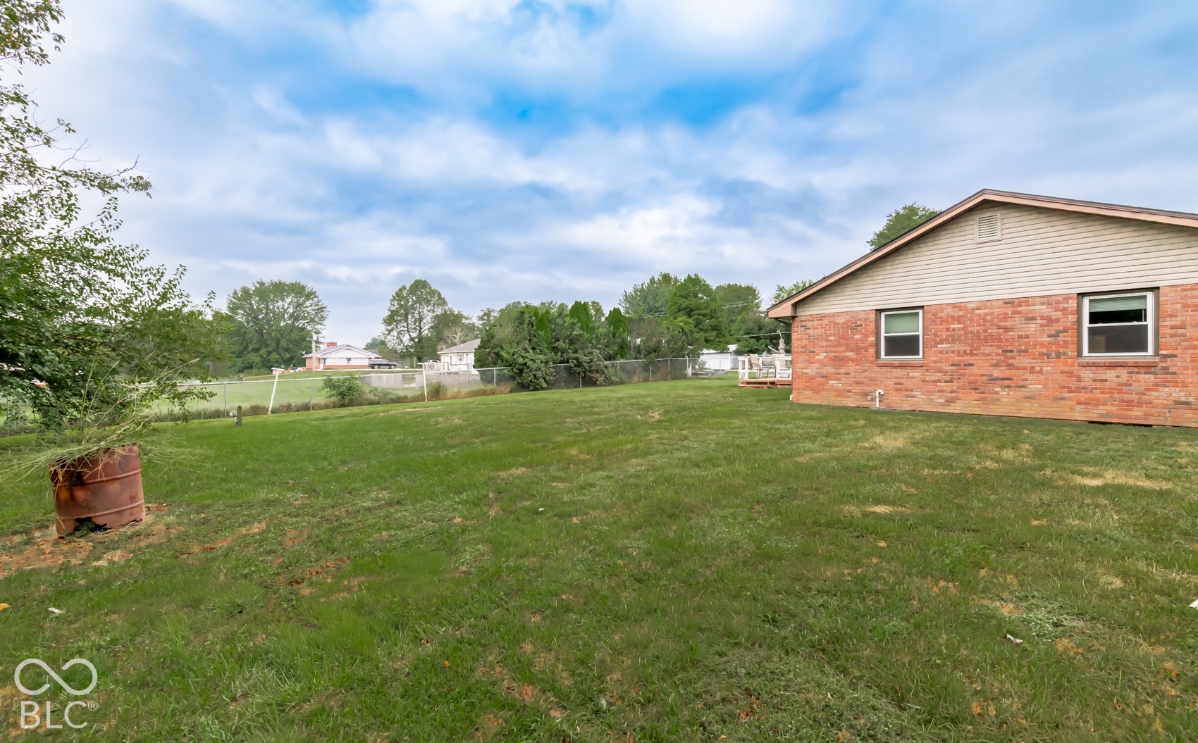 Expansive grassy yard with mature perimeter trees, featuring a red brick exterior with siding, and a rear deck