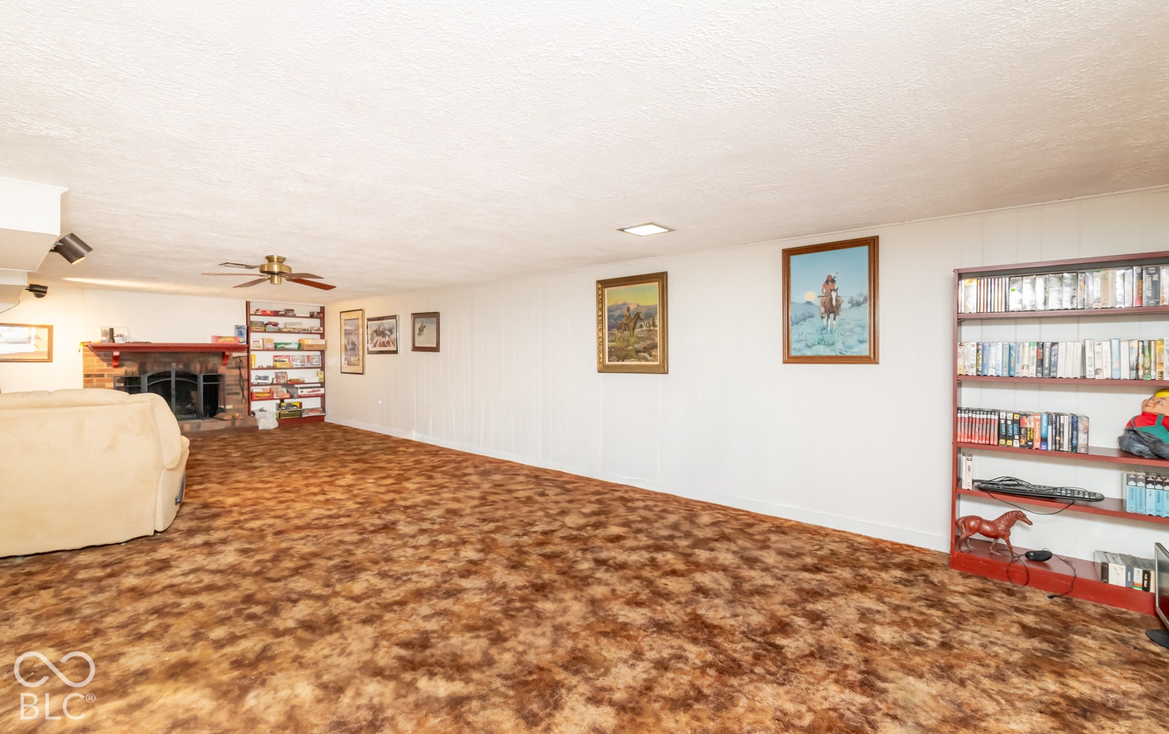 Spacious recreational room featuring a stone-clad fireplace with a hearth, a ceiling fan with integrated lighting, and track lighting fixtures