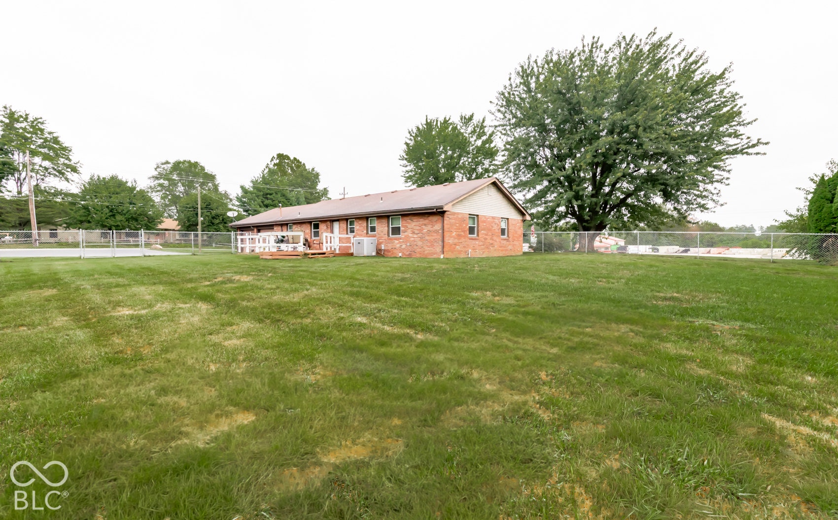Expansive grassy yard with mature trees, a brick exterior building, and an elevated wood-finish deck with white railings