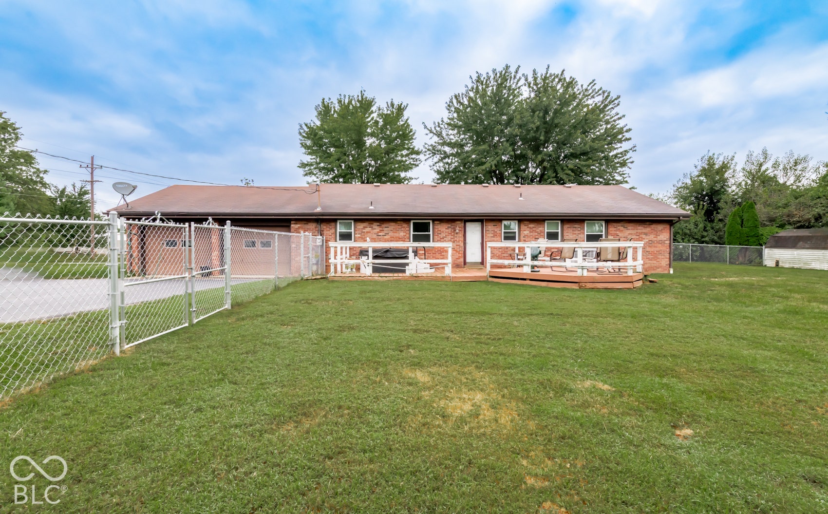 Expansive backyard with a manicured lawn, multi-level wood deck, and full perimeter chain link fencing