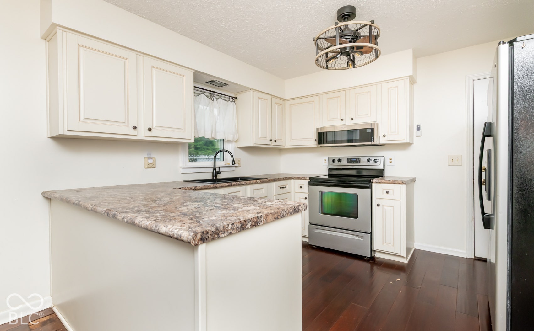 White cabinetry with dark hardware, stainless steel appliances, dark wood-finish flooring, and a ceiling fan with integrated lighting