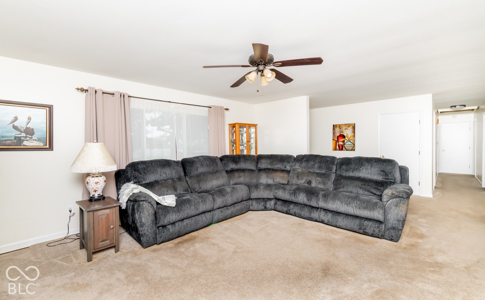 Carpeted living area featuring a ceiling fan with integrated lighting and a window with curtain rod and drapes