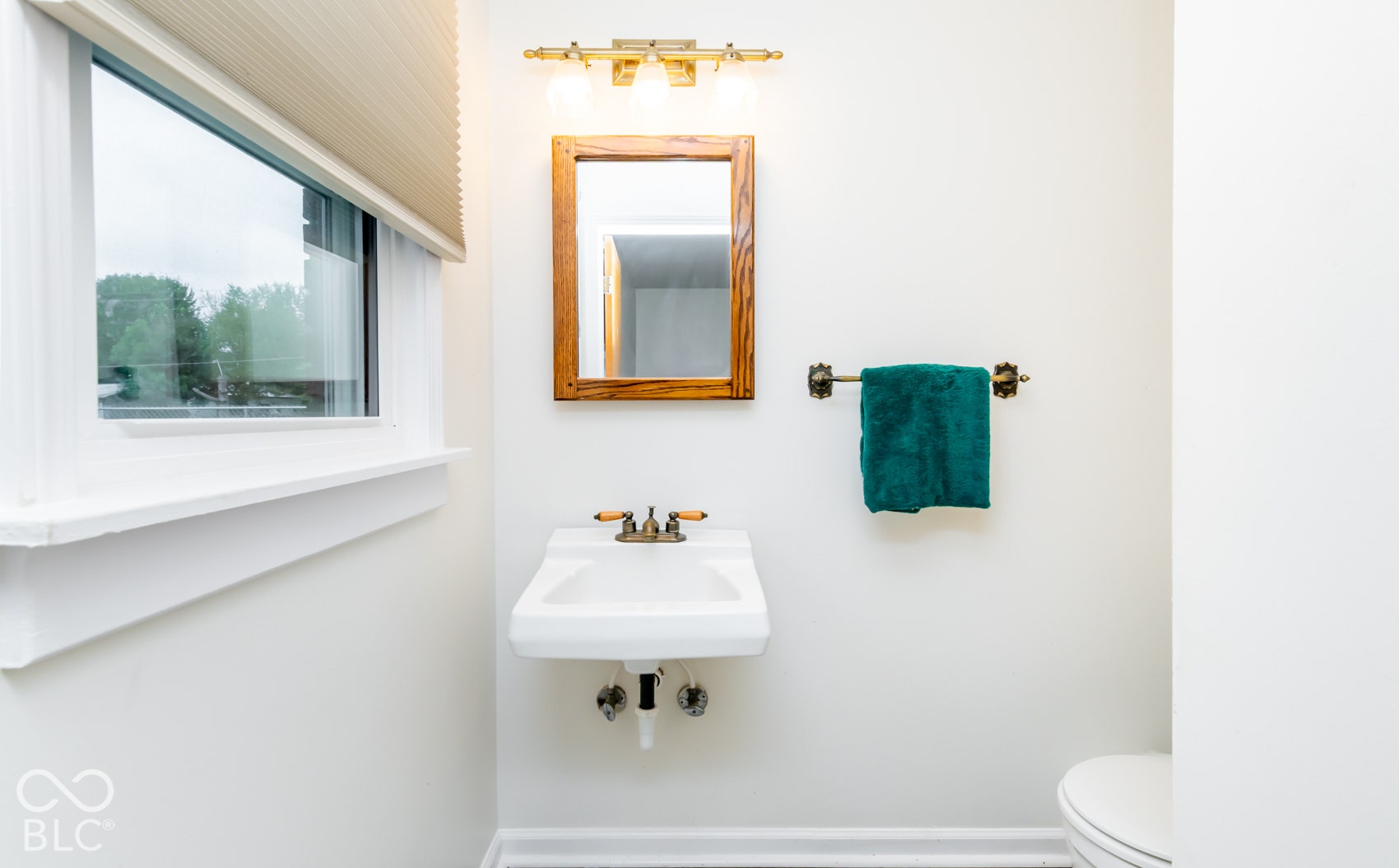 Wall-mounted sink with brass-finish faucet, framed mirror, and two-light vanity fixture
