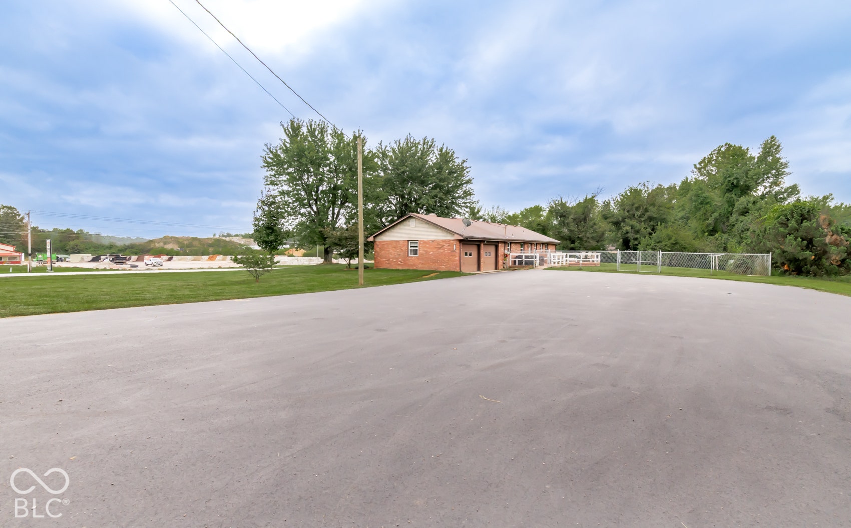 Expansive paved lot with a brick building featuring multiple garage doors and a white fence
