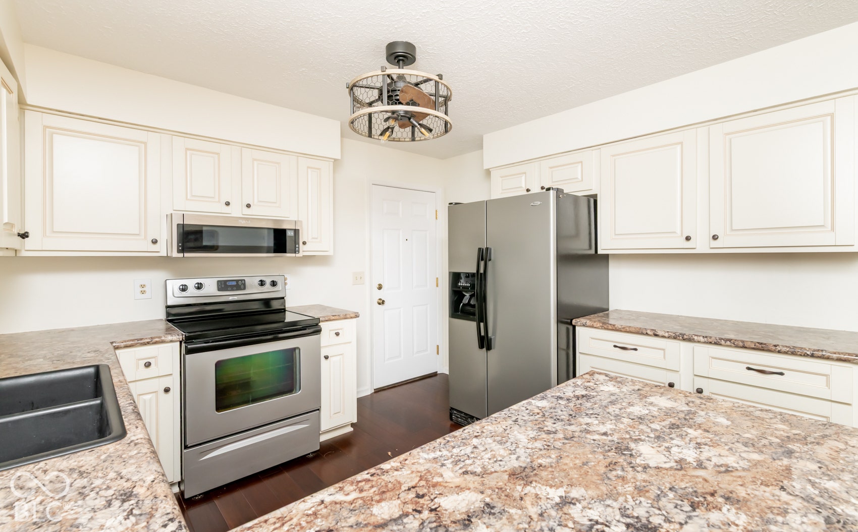 White paneled cabinetry, stainless steel appliances, speckled countertops, wood-finish flooring, and a decorative ceiling light fixture